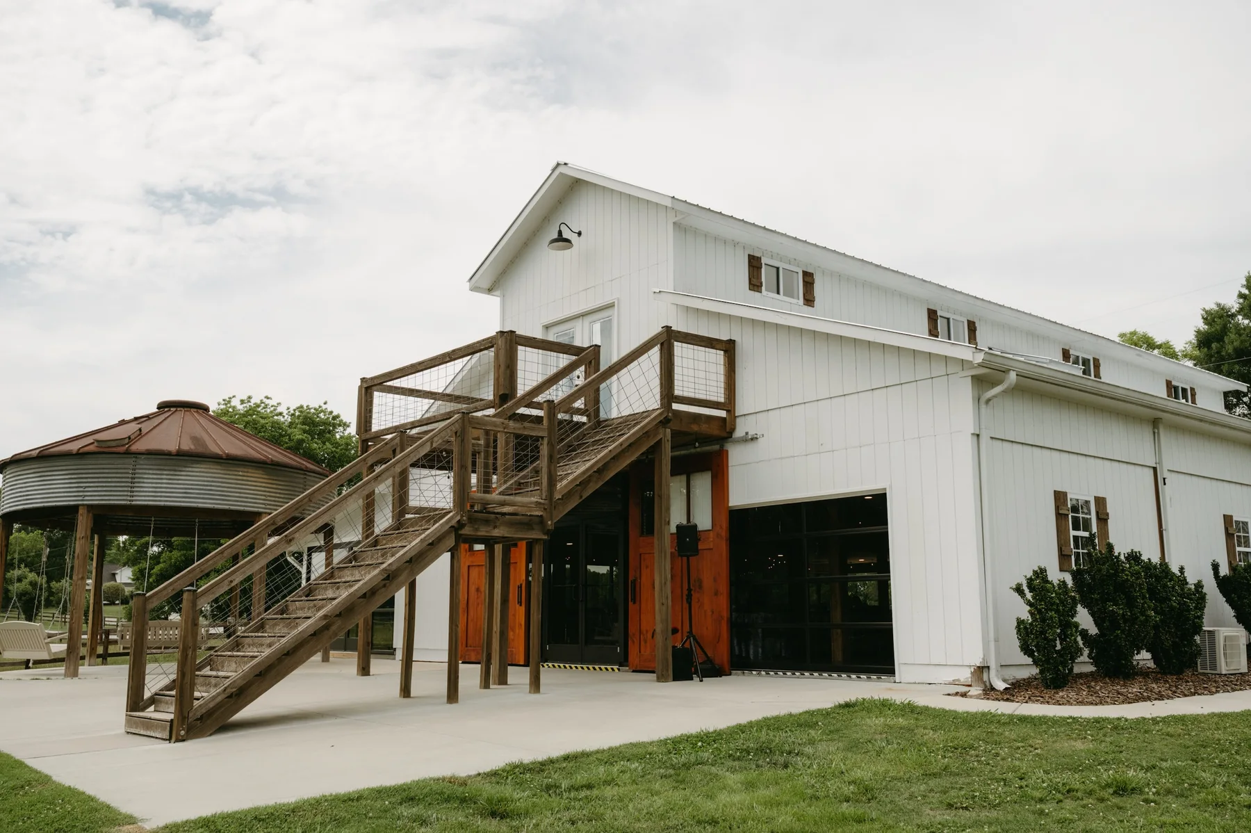 The white barn with its exterior staircase and open wood doors, the silo swings beside it, under a soft overcast sky