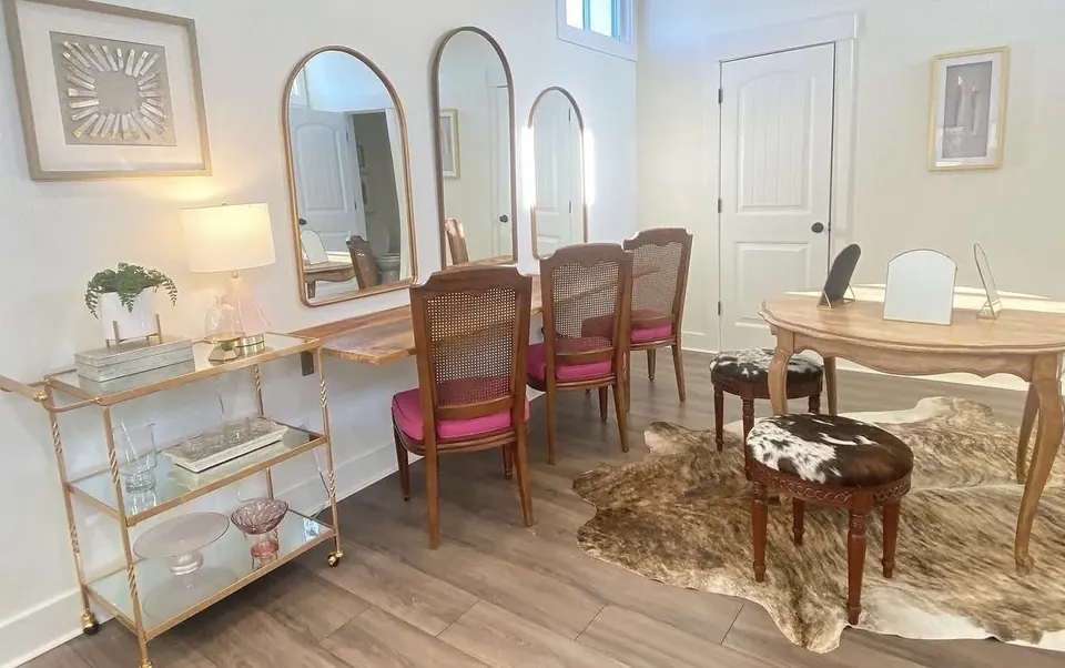 Three arched gold mirrors over a wood vanity counter with pink-cushioned chairs and a gold bar cart in the bridal suite