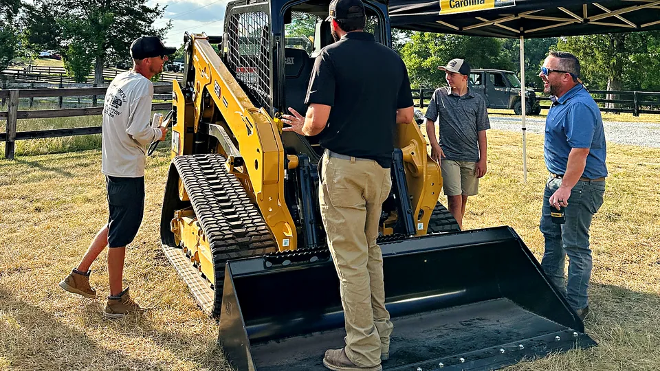 Guests gathered around a compact track loader during an outdoor equipment demo