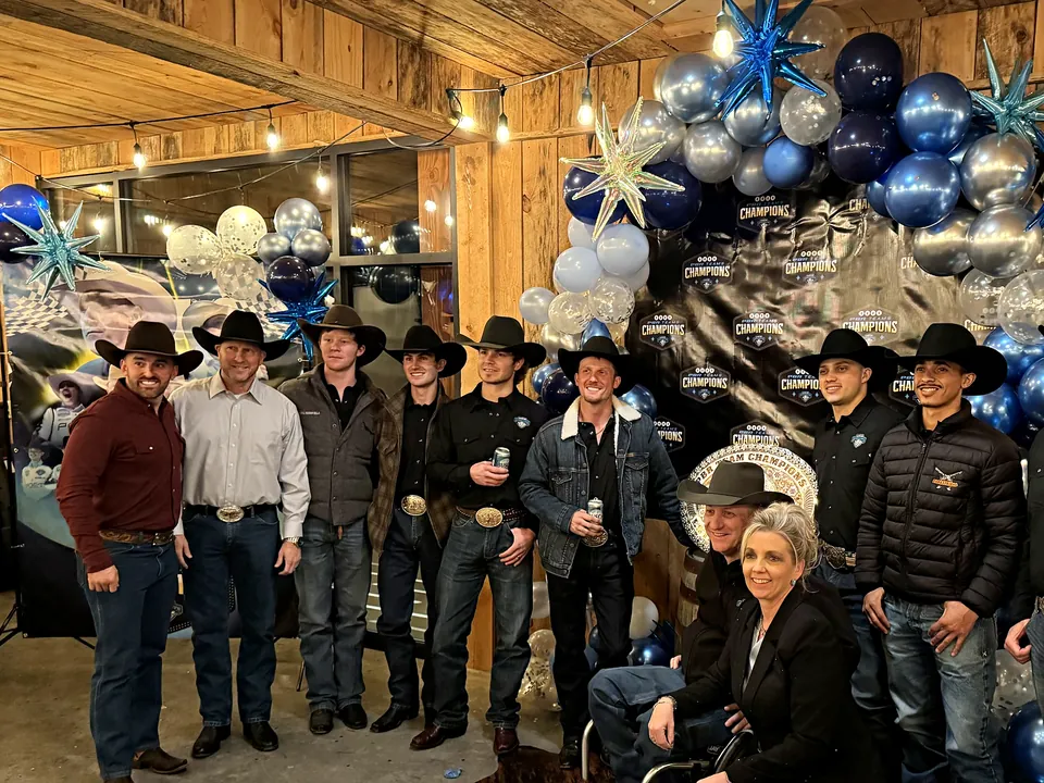 A professional bull riding team posing together at their championship celebration in the barn