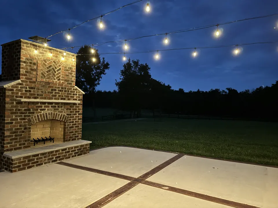 Brick fireplace beneath string lights against an evening sky