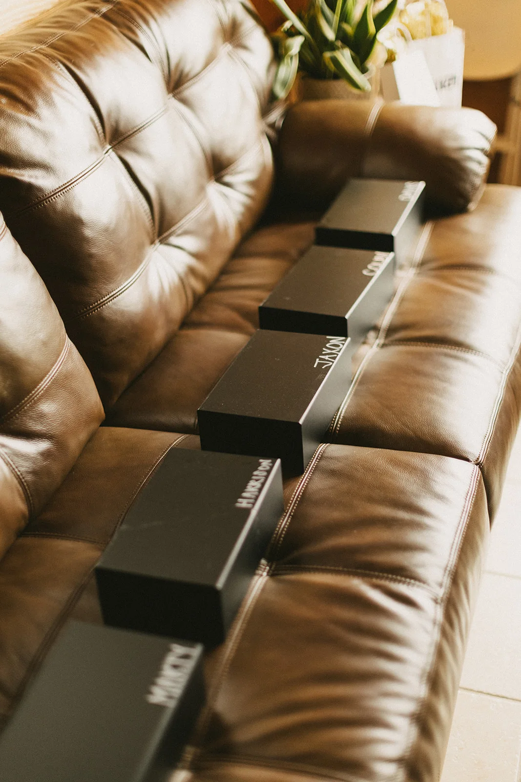A tufted brown leather sofa in the groom suite with gift boxes lined along its back