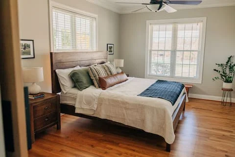 A king bed in a bright room with wood floors and corner windows