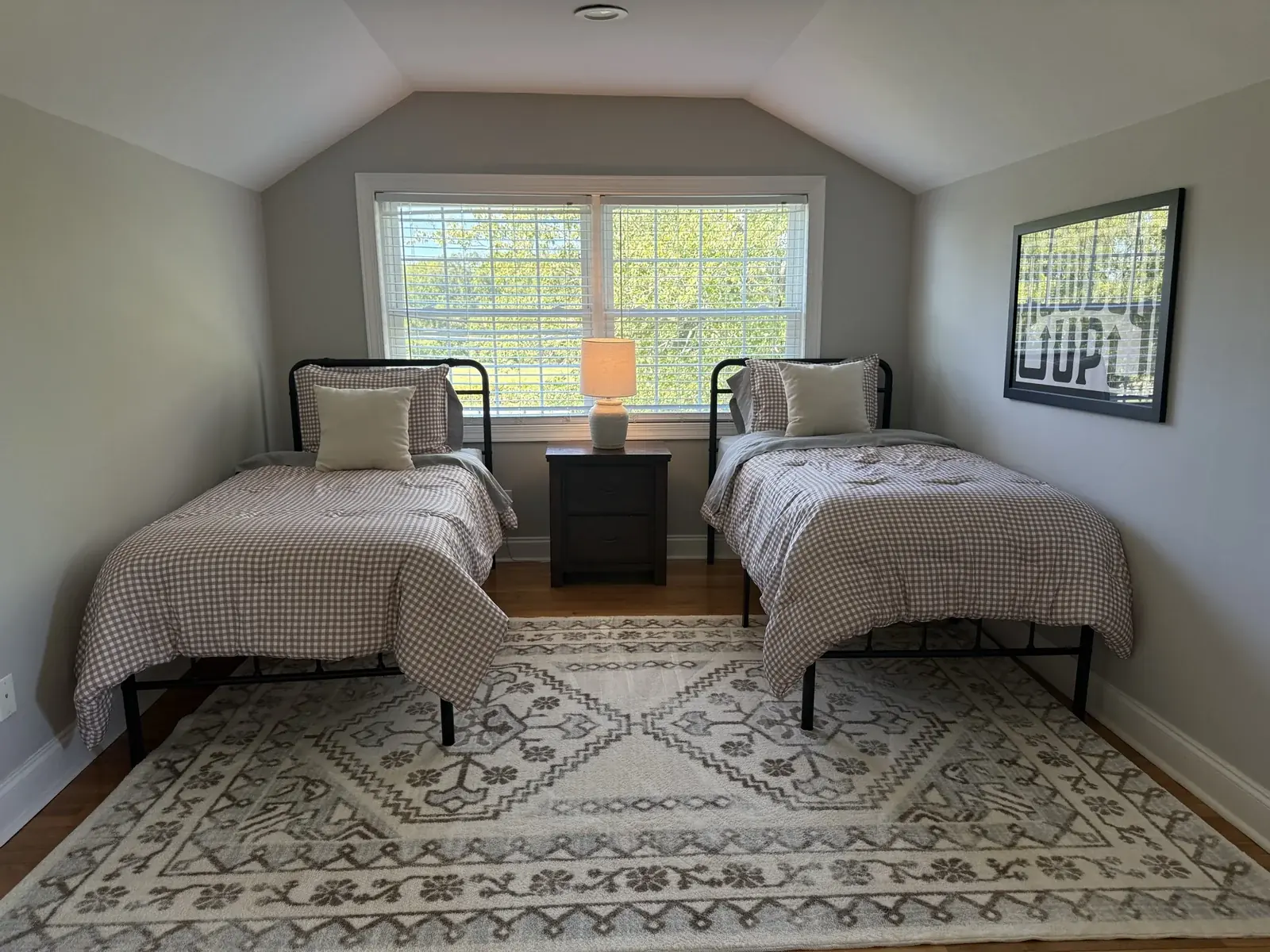 Two separate twin beds with checked bedding, a shared nightstand, and a large window in the loft