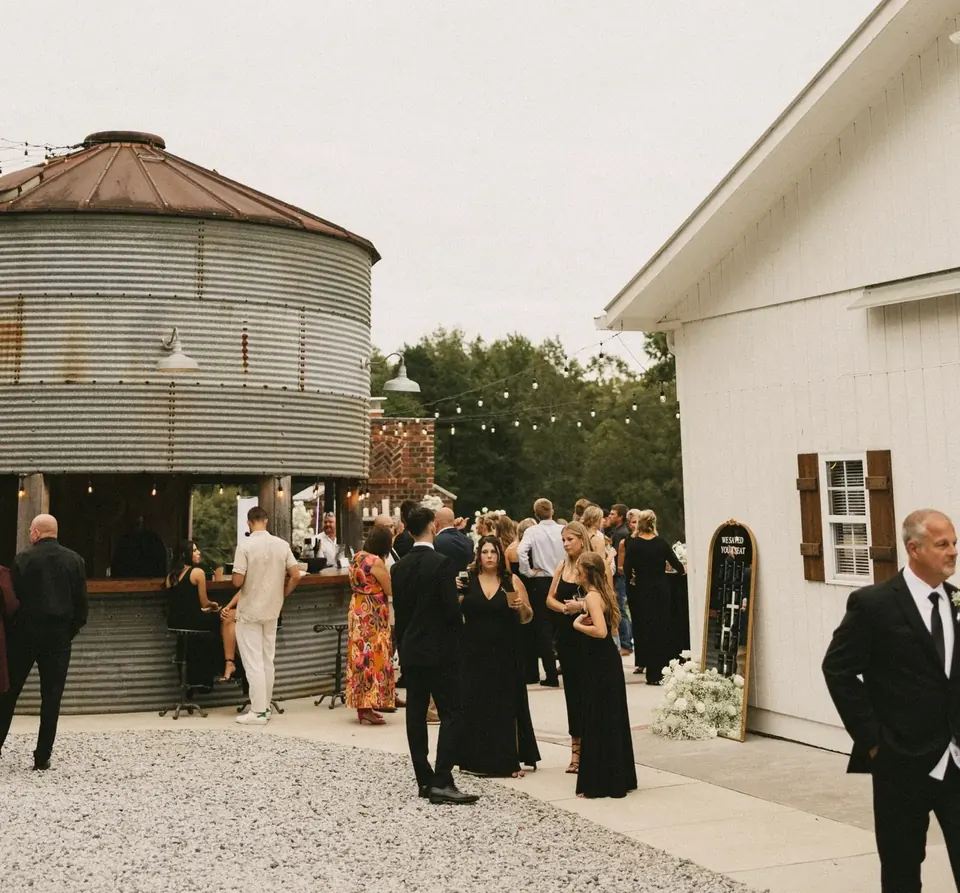 Wedding guests mingling on the patio between the Silo Bar and the white barn beneath string lights