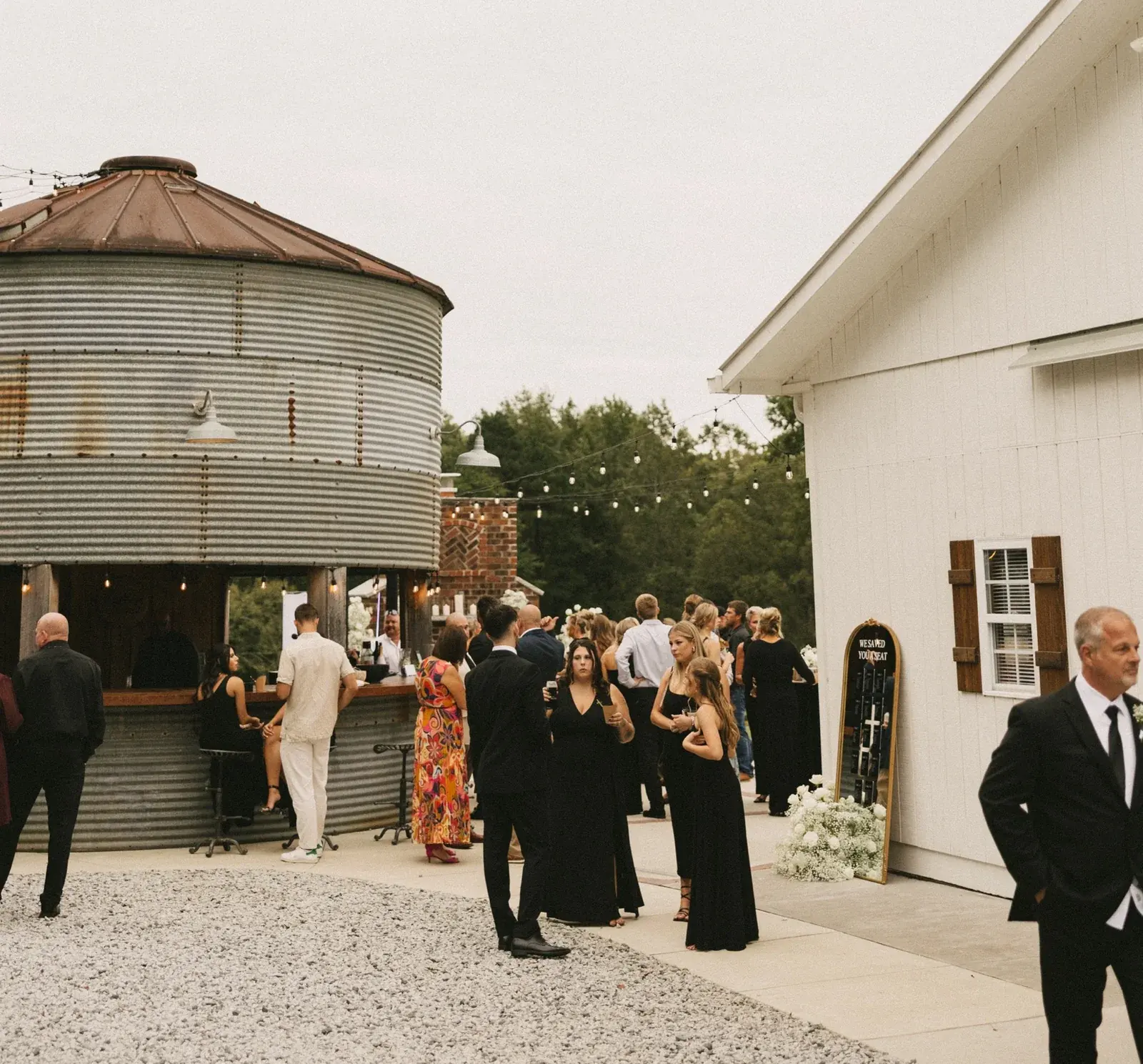 Wedding guests mingling on the patio between the Silo Bar and the white barn beneath string lights