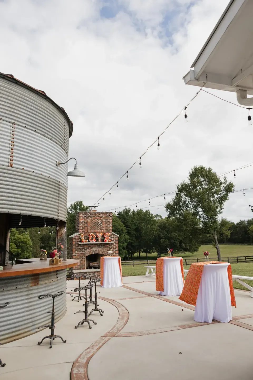 The Silo Bar with tractor-seat stools, cocktail tables in orange linens, and the brick outdoor fireplace under string lights
