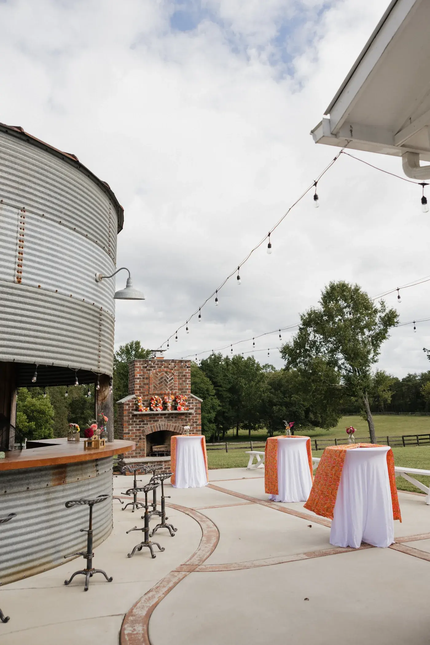 The Silo Bar with tractor-seat stools, cocktail tables in orange linens, and the brick outdoor fireplace under string lights
